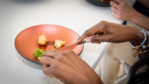 Close-up image of hands cutting slicing into food on an elegant dish on a white tablecloth